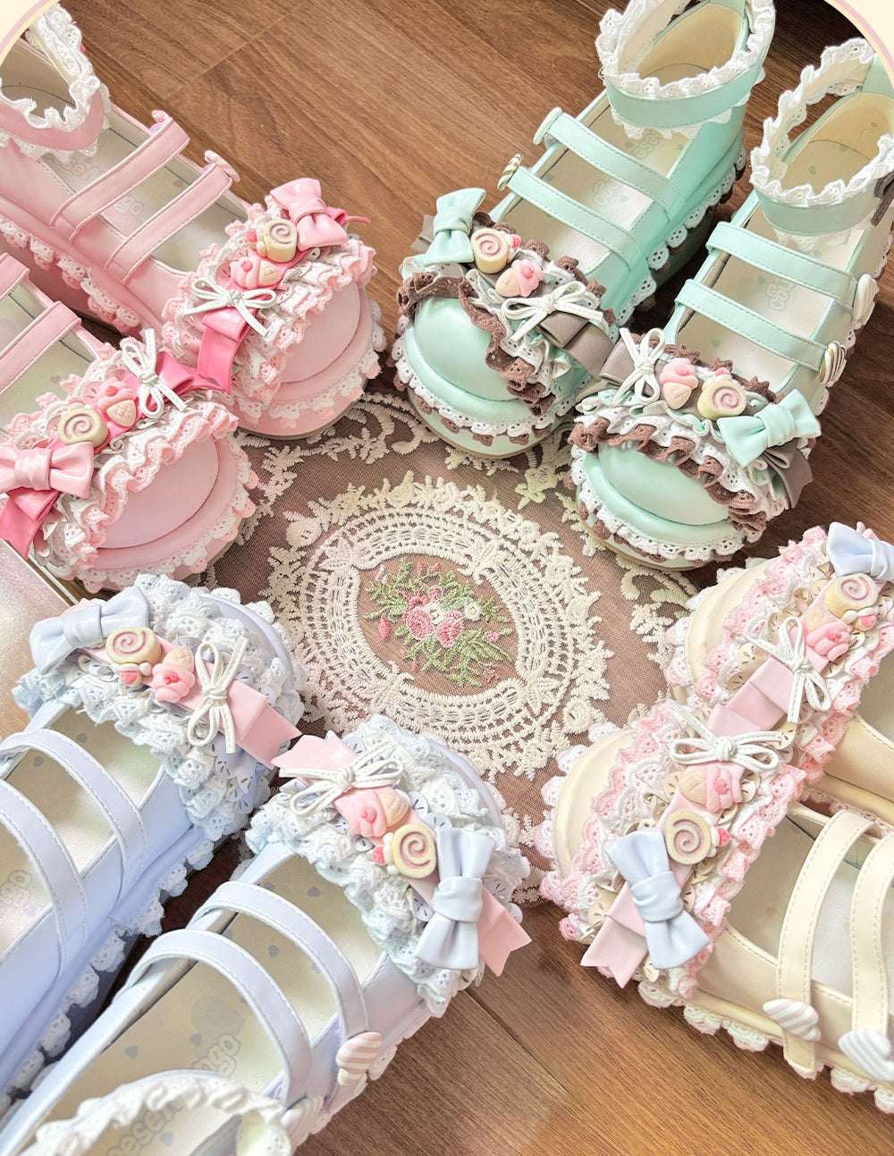 Pastel-colored lolita shoes with decorative flowers and bows on a wooden surface.