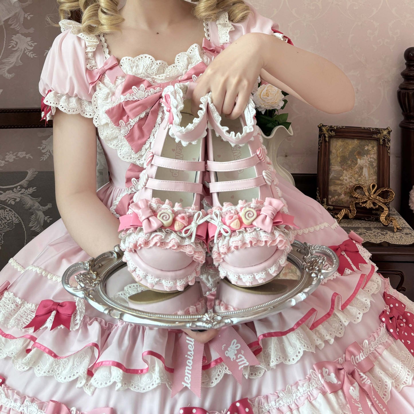 Person in a pink and white dress holding a pink shoe on a silver tray.