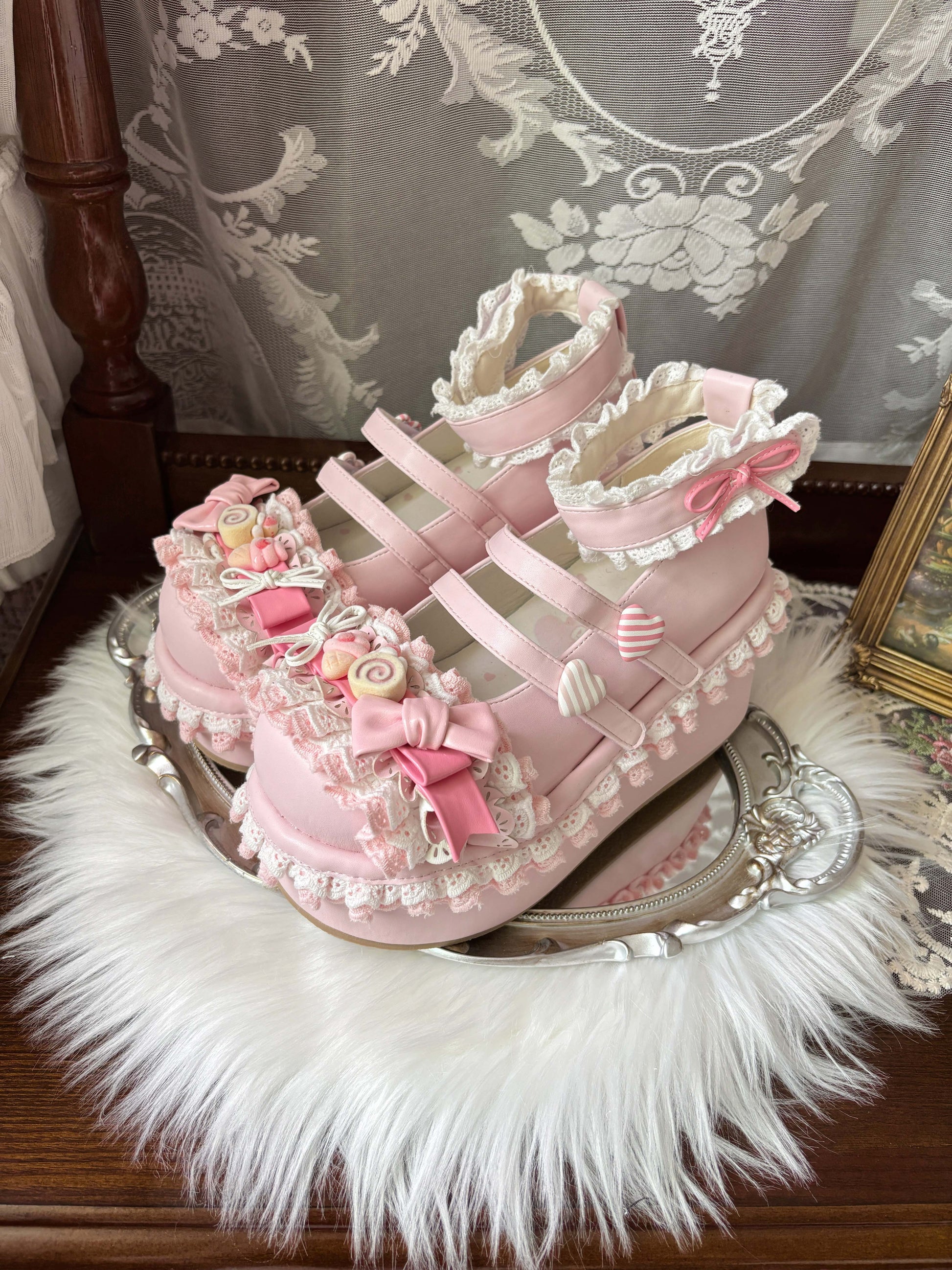 Pink decorative shoes with lace and bows on a white fur surface.