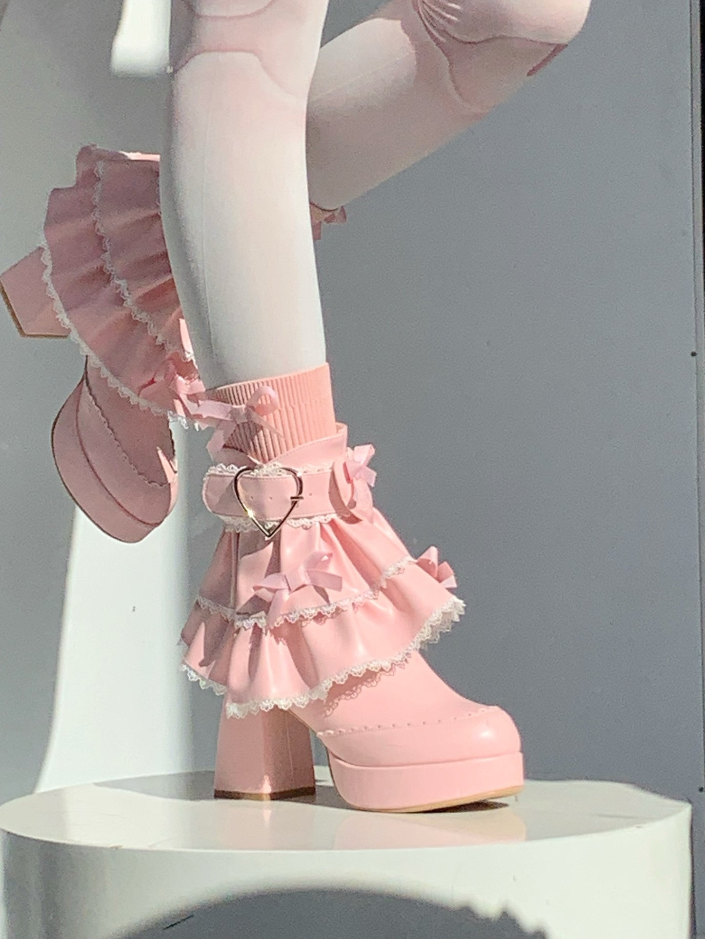 Pink ruffled platform shoes with a heart detail on a neutral background
