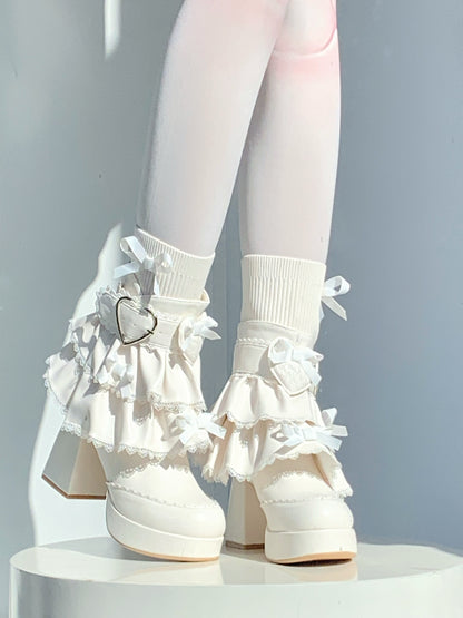White platform shoes with ruffles and a heart charm on a plain background