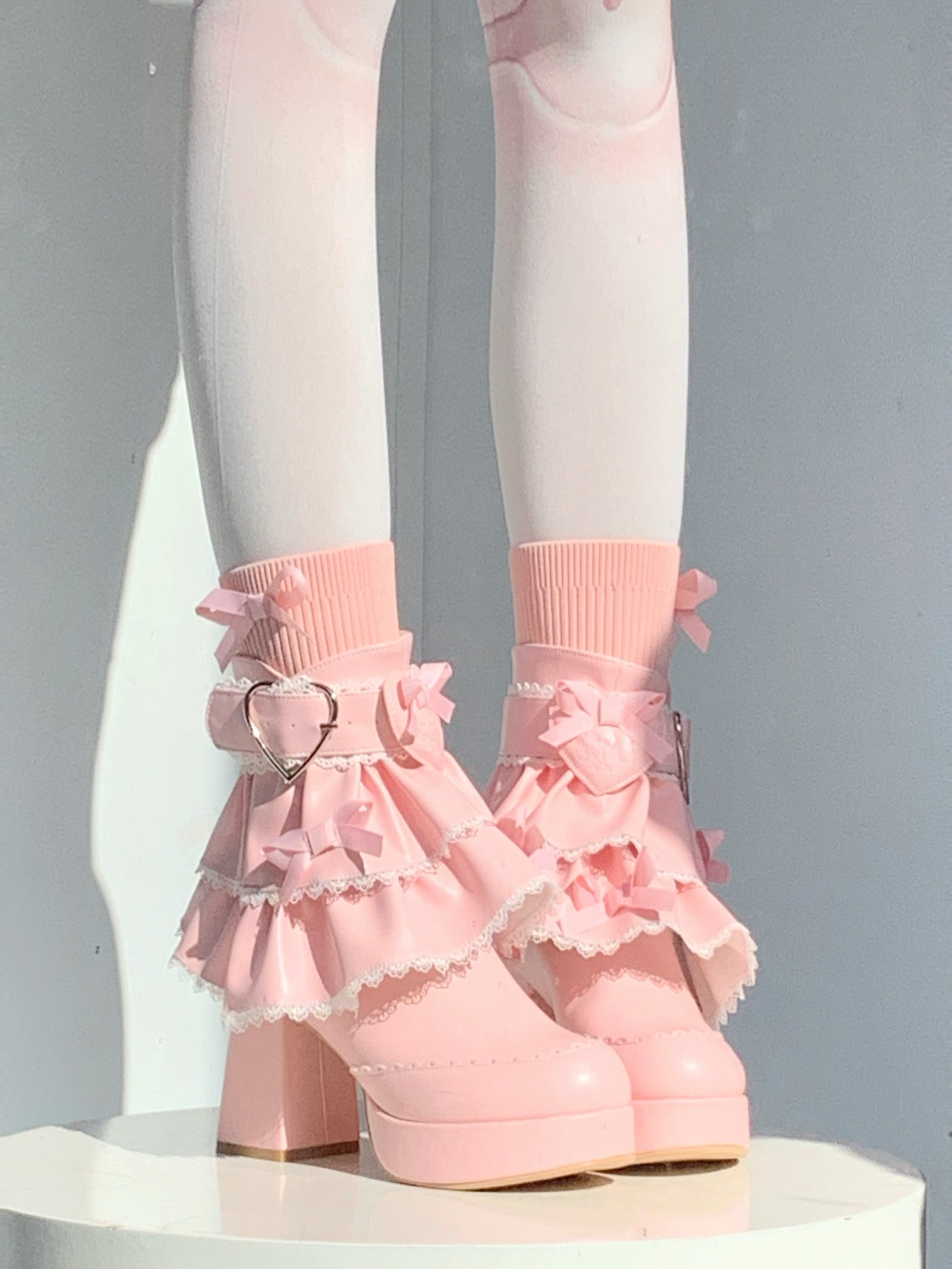Pink ruffled boots with heart details and pink shoes on a neutral background