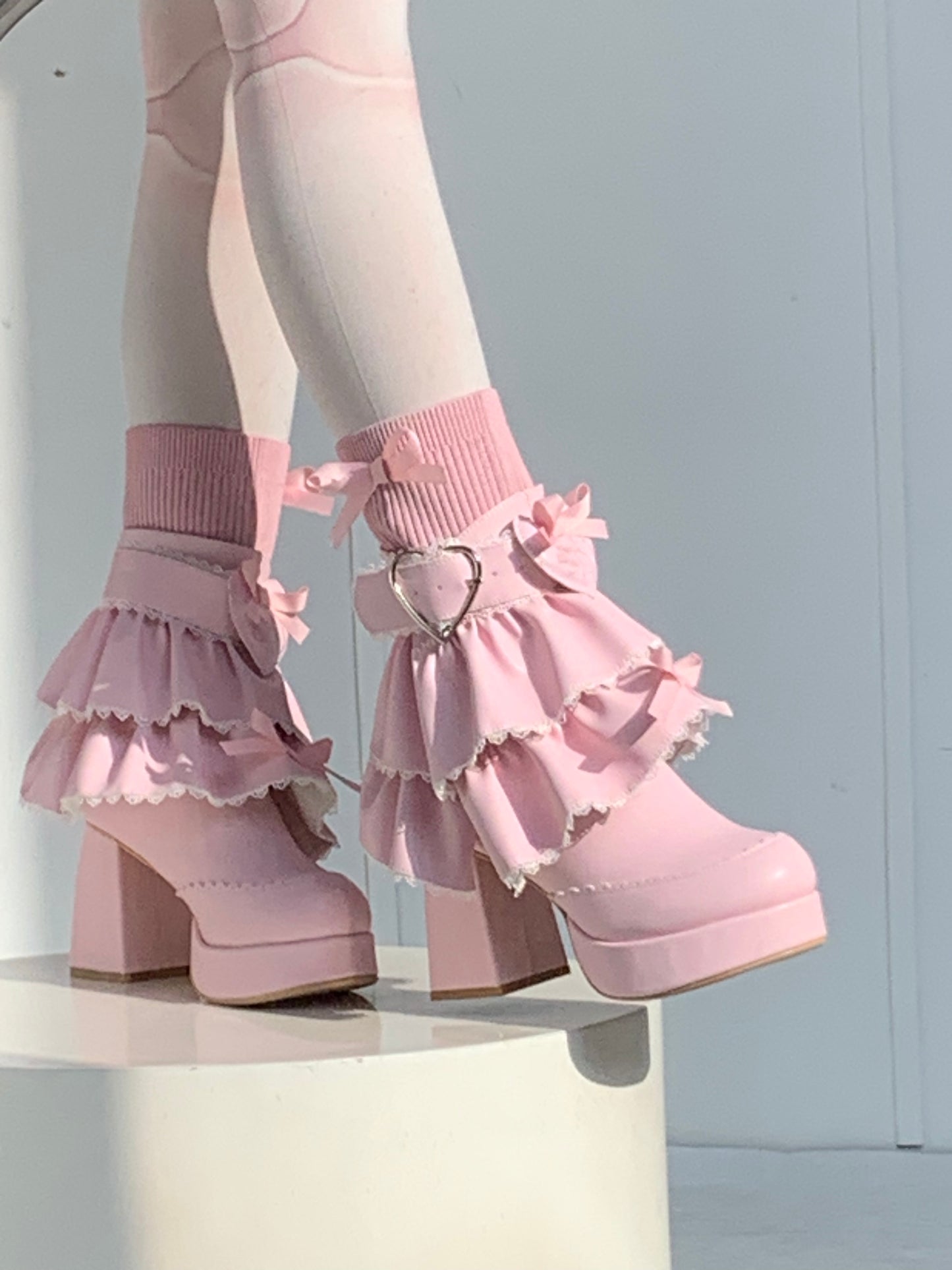 Pink high-heeled shoes with ruffled details on a reflective surface.