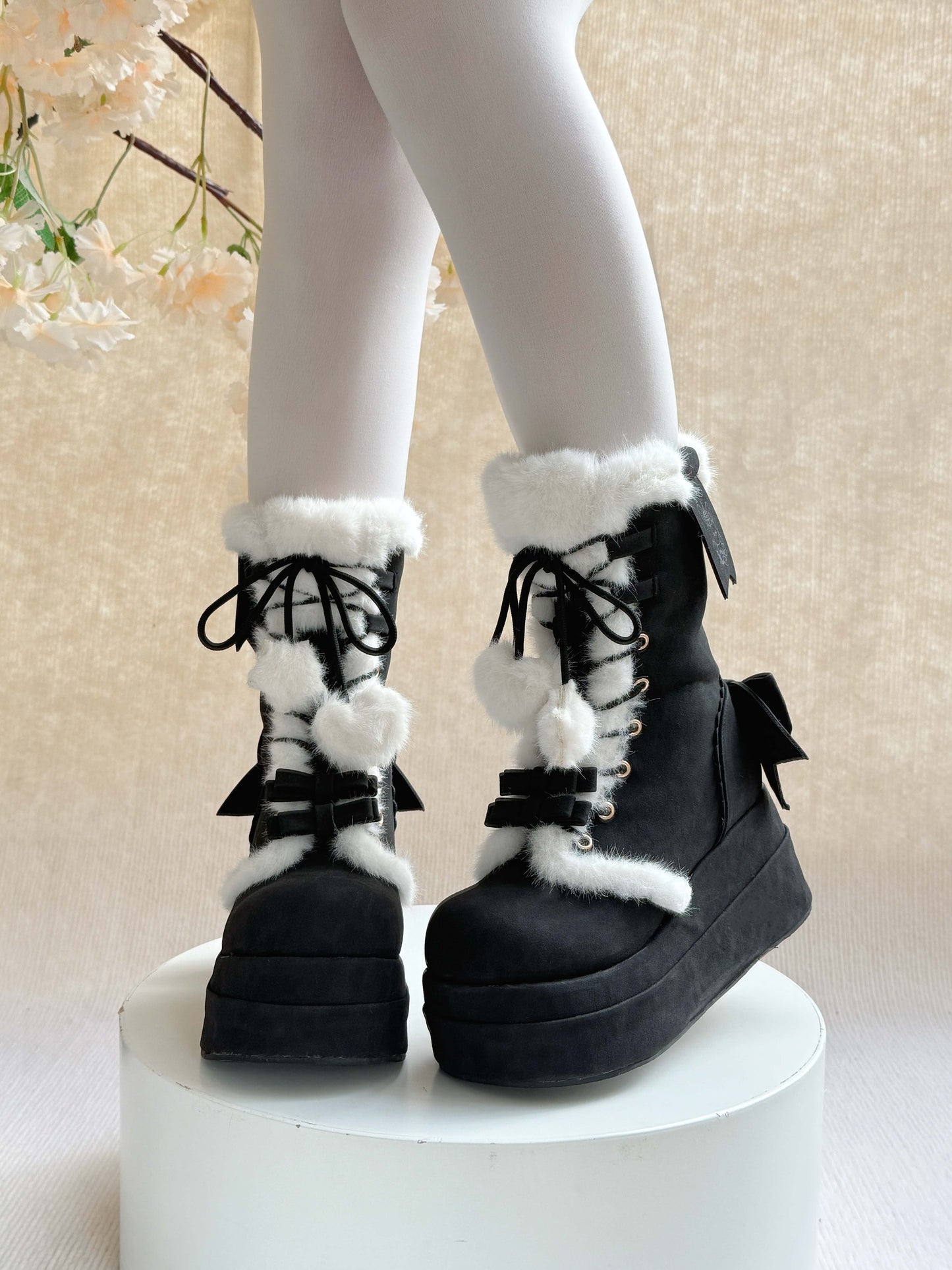 Black platform winter boots with white fur and bows on a neutral background