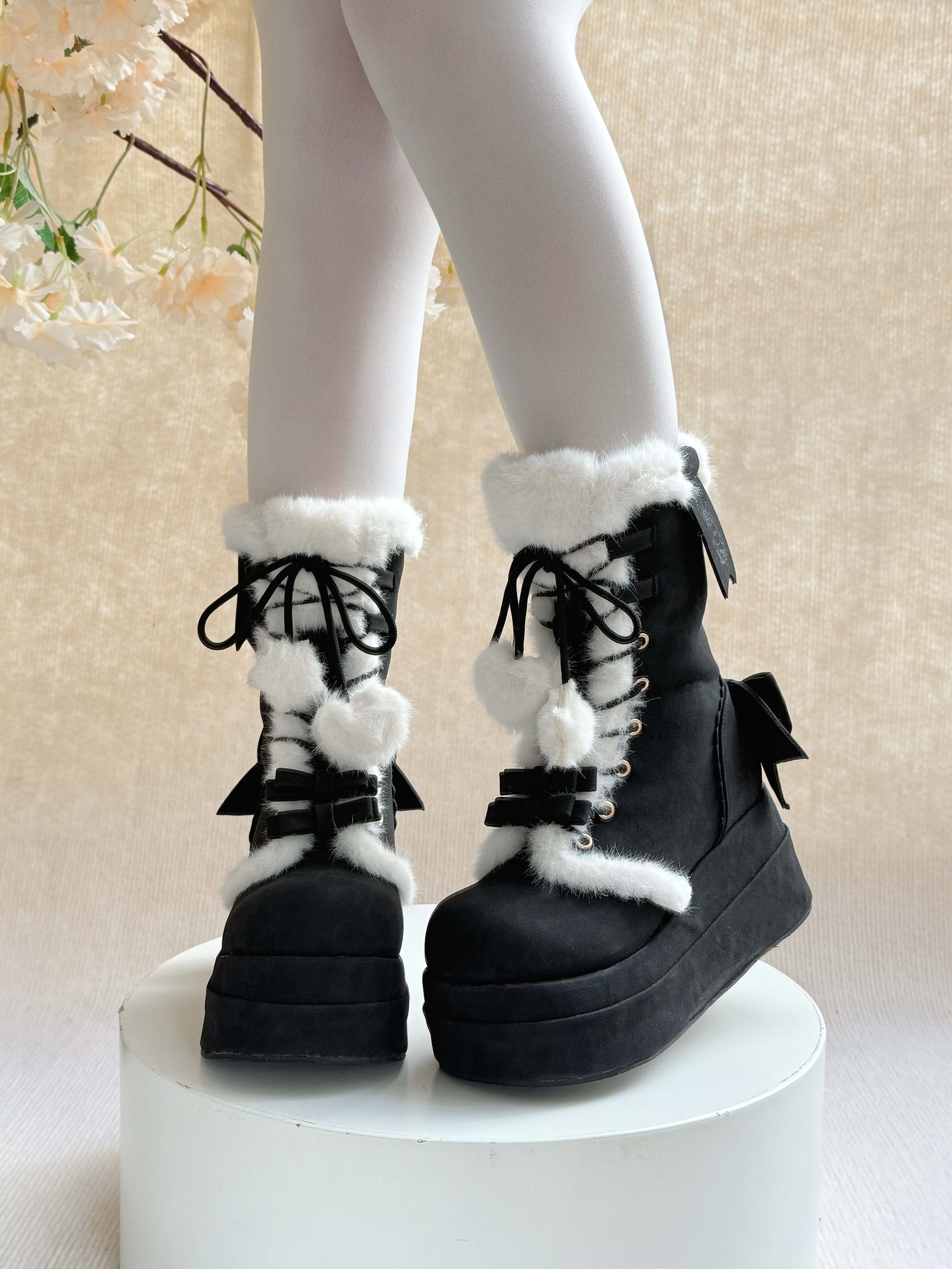 Black platform winter boots with white fur and bows on a neutral background