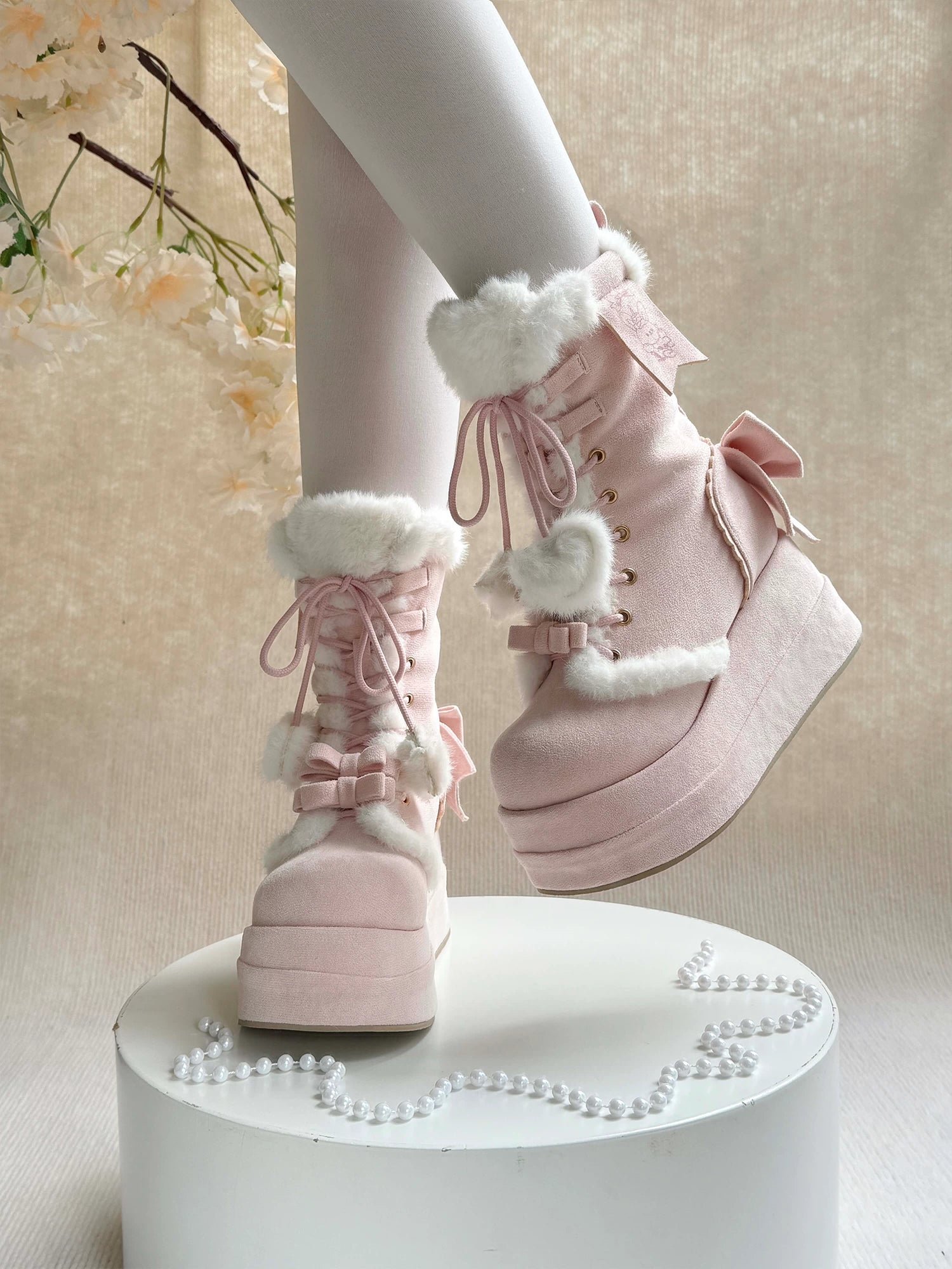 Pink boots with white fur and bows on a white pedestal against a light background