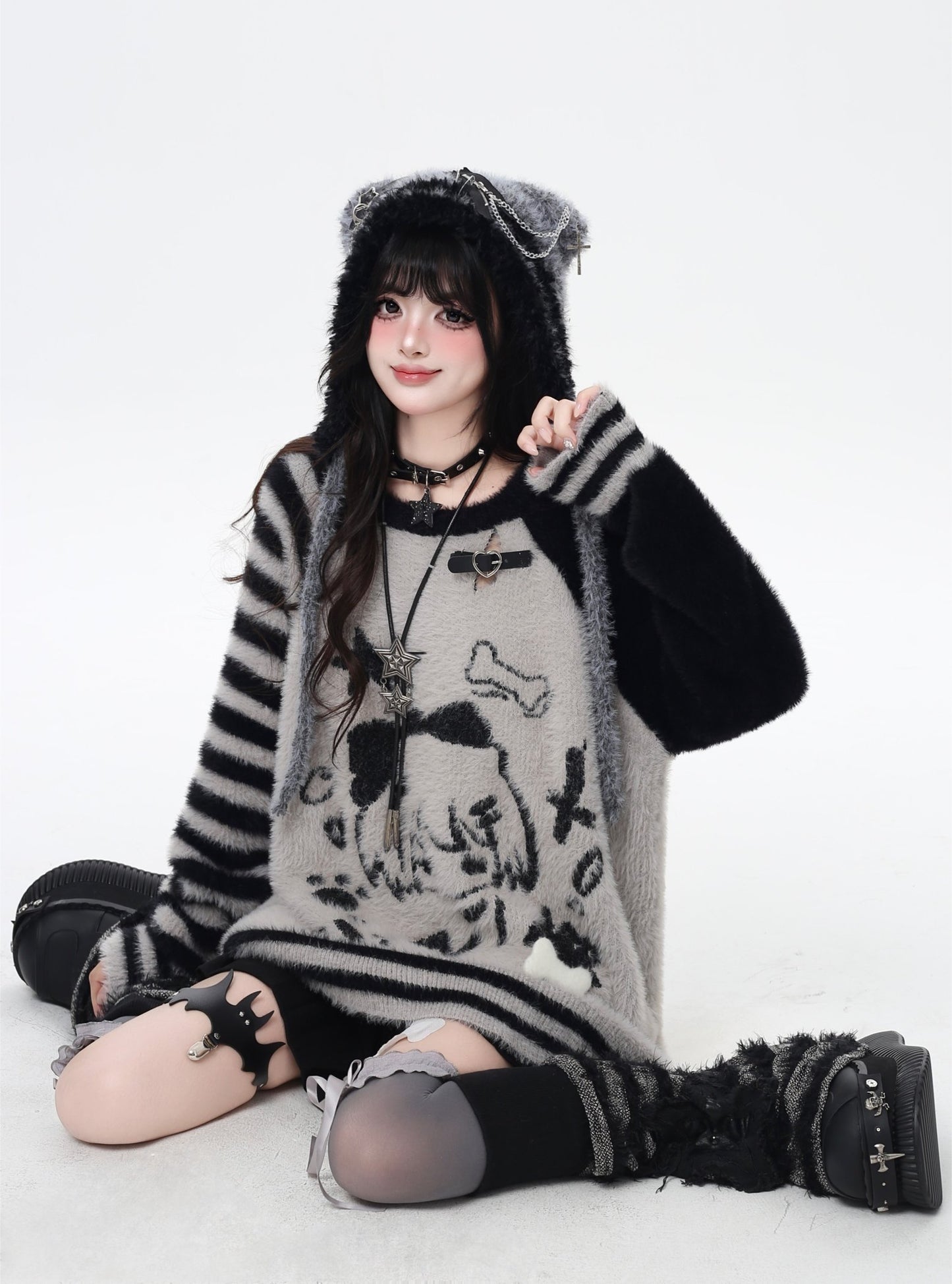 Person wearing a black and gray striped sweater with a hood, sitting on a white background.