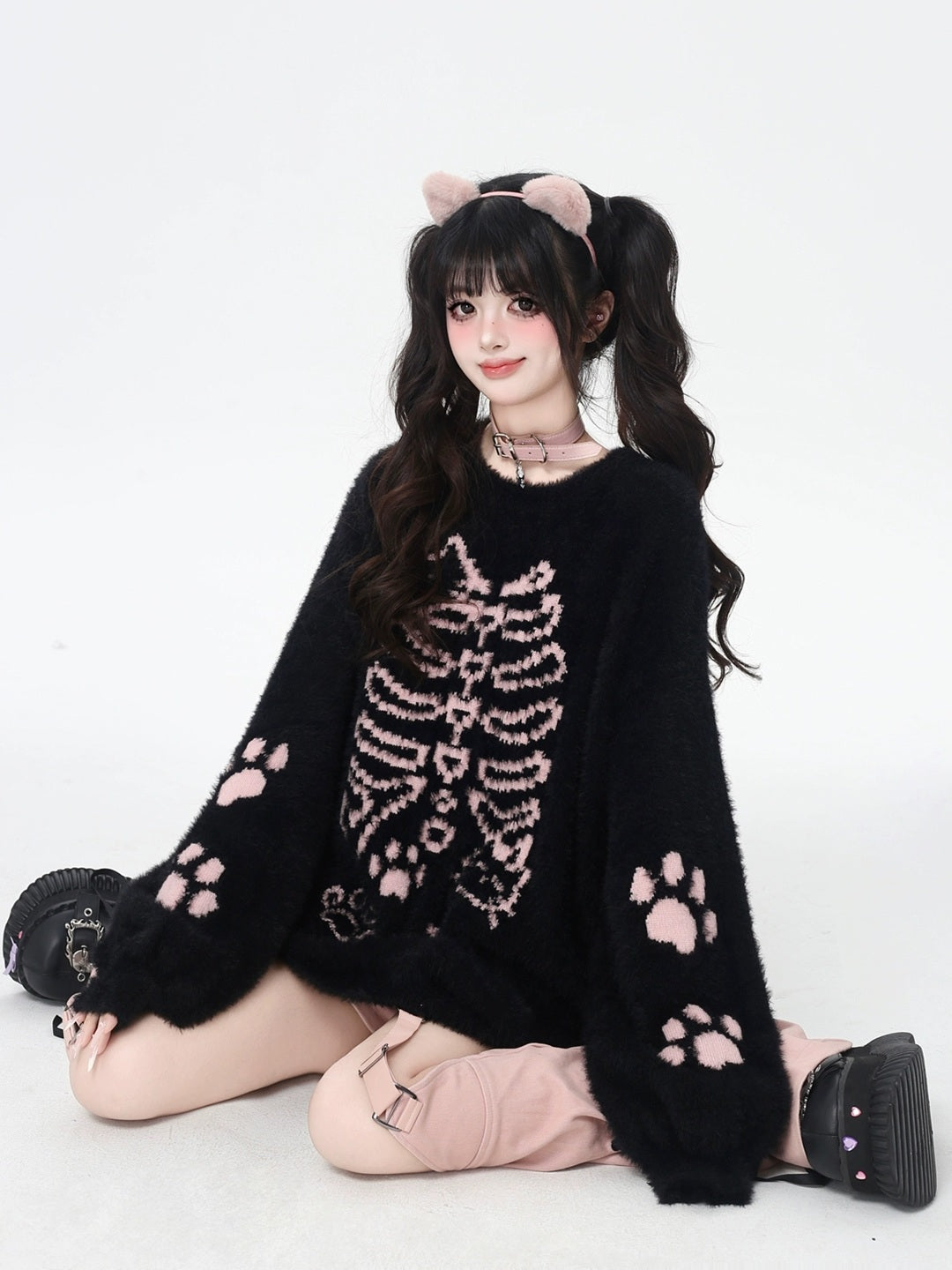 Person wearing a black sweater with pink skeleton and paw patterns on a white background