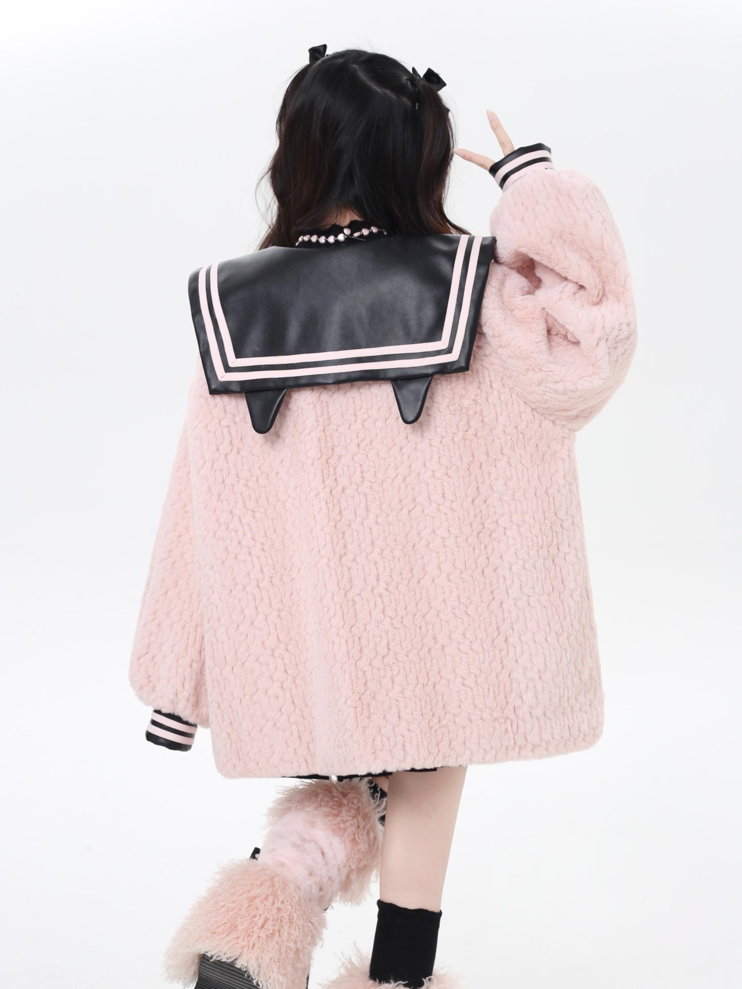 Person wearing a pink fluffy coat with a black and white trim on a white background