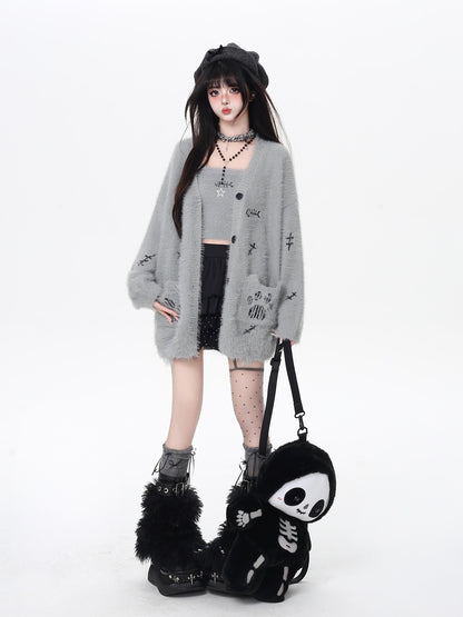 Person wearing a gray cardigan with skull designs, holding a black bag with a skull design on a white background.