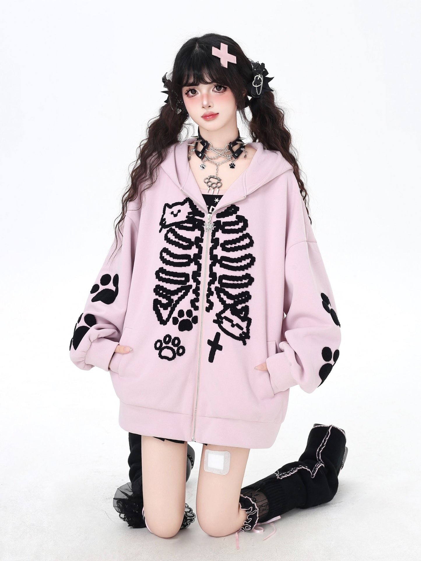 Person wearing a pink hoodie with black skeleton and paw print designs on a white background