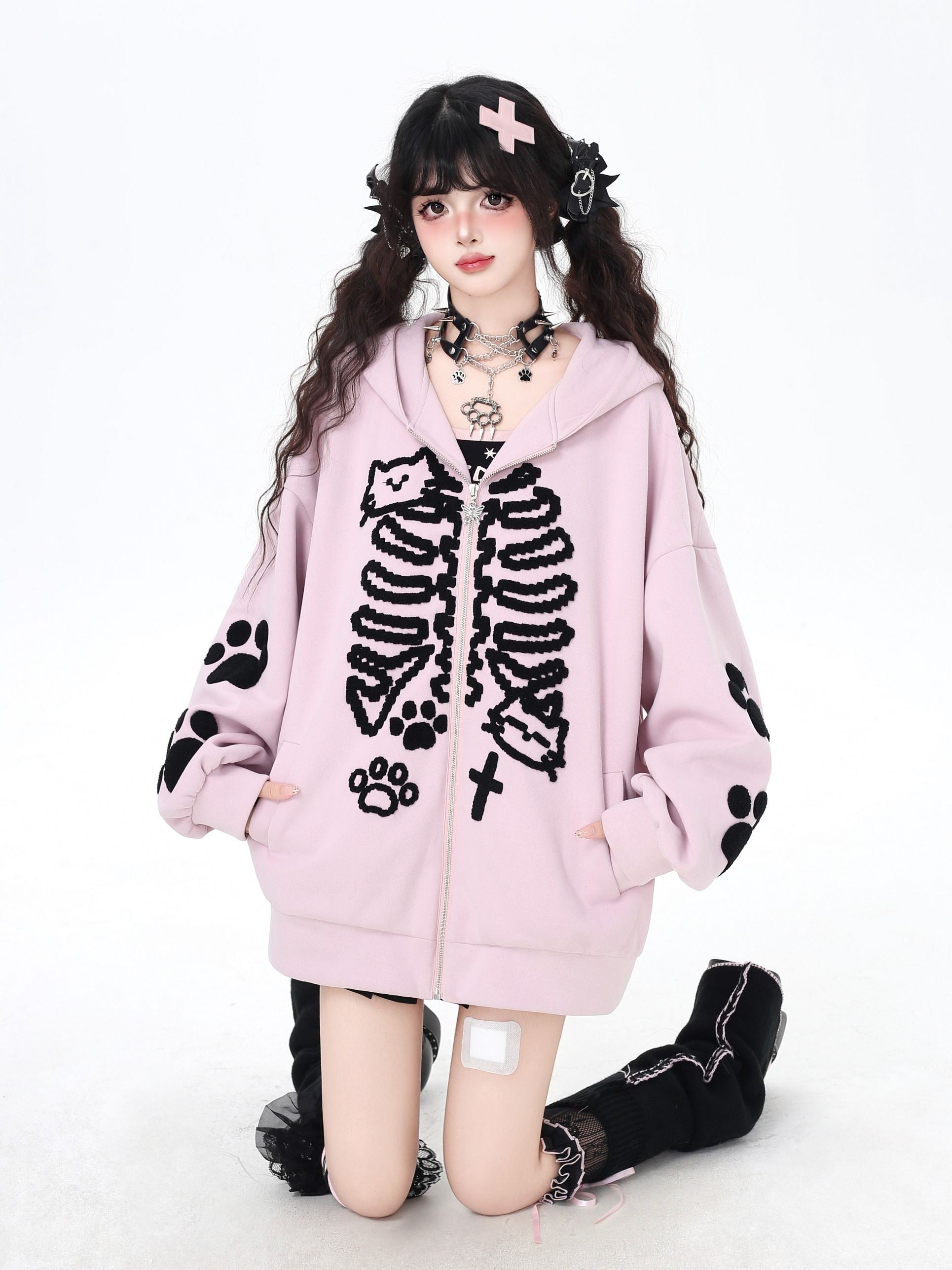 Person wearing a pink hoodie with black skeleton and paw print designs on a white background