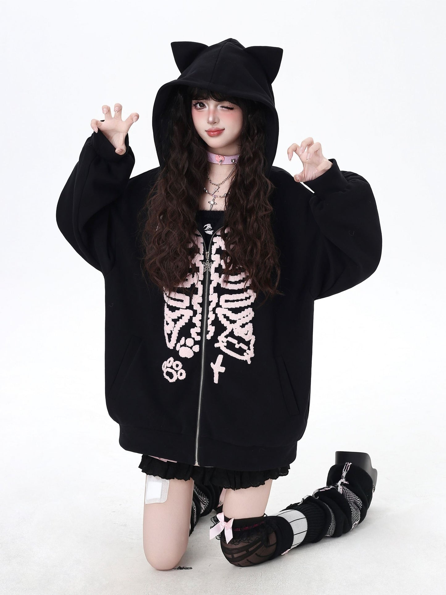 Person wearing a black hoodie with cat ears and skeleton design on a white background