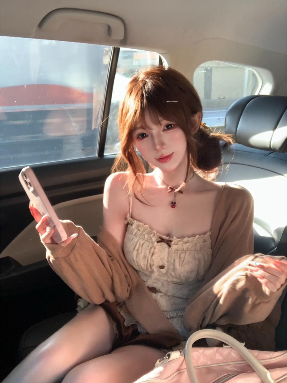 Woman sitting in a car holding a phone, wearing a coquette beige outfit.