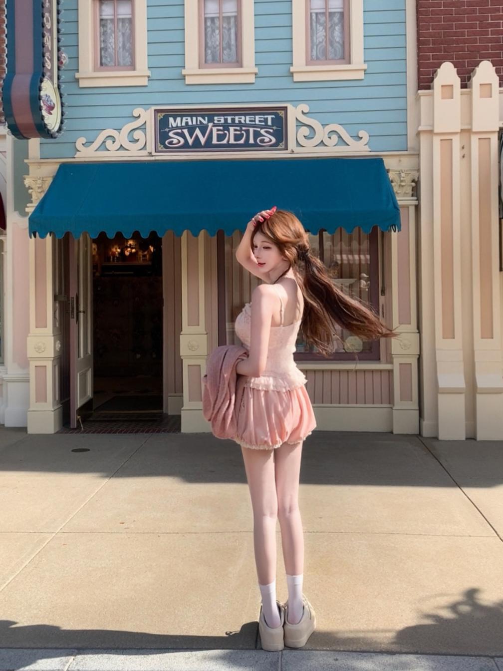Woman in a coquette pink dress standing in front of a building with a blue awning.
