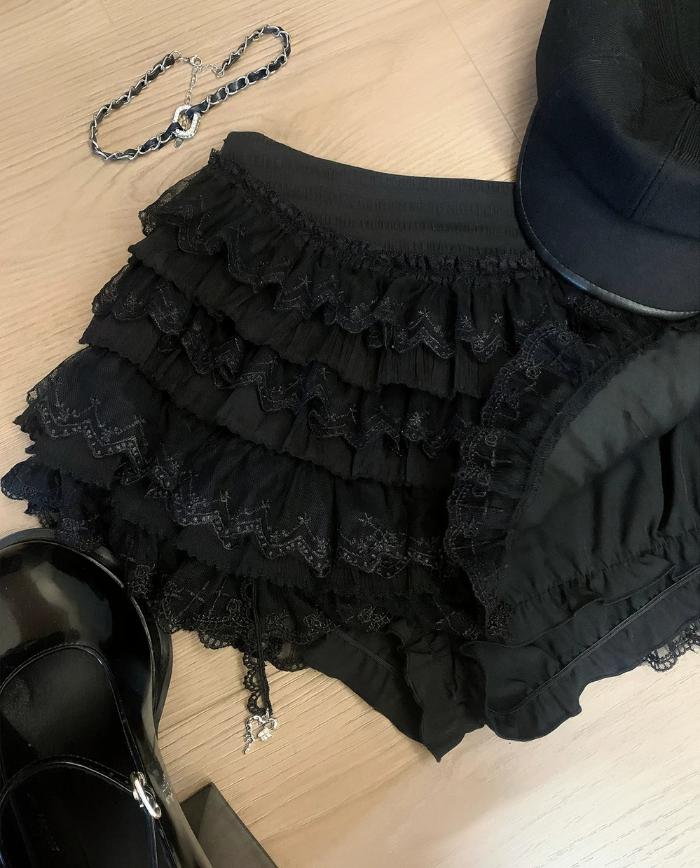 Black ruffled skirt with a chain, black shoes, and a black hat on a light wooden surface.