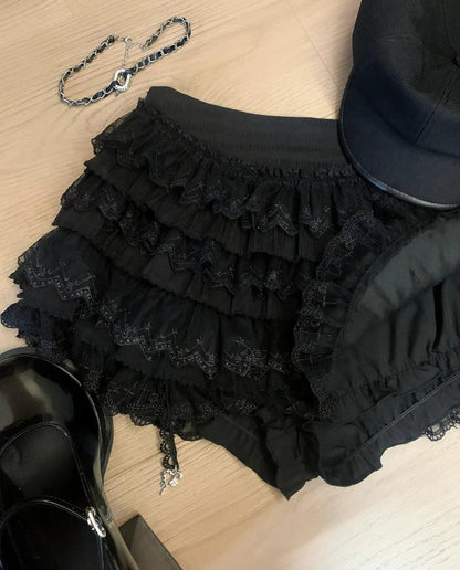 Black ruffled skirt with a chain, black shoes, and a black hat on a light wooden surface.