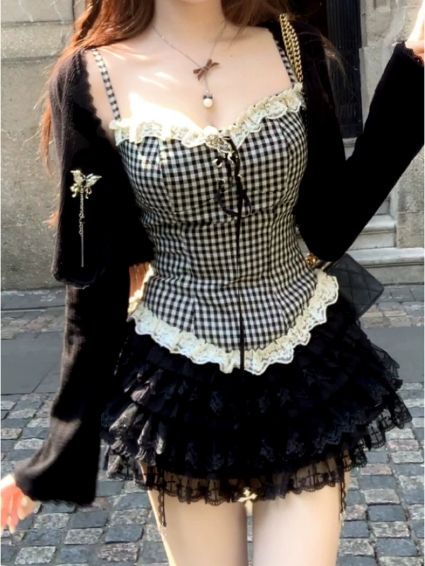 Person wearing a dark coquette black and white checkered dress with lace details on a stone pavement.