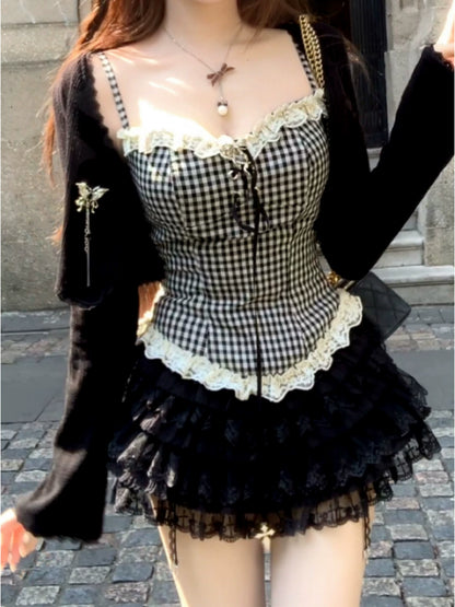 Person wearing a dark coquette black and white checkered dress with lace details on a stone pavement.