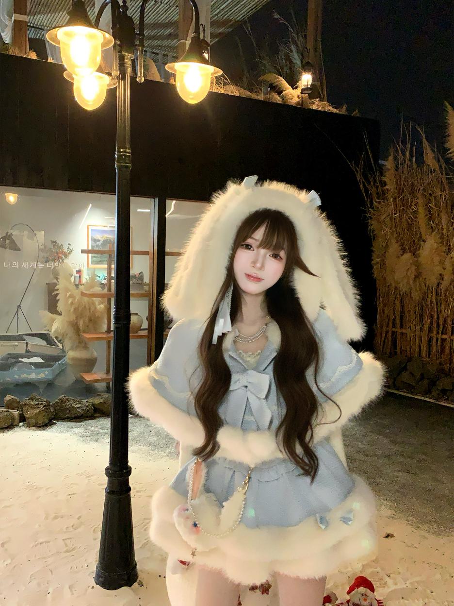 Person wearing a fluffy white hooded rabbit ears blue coat in an indoor setting with decorative elements.