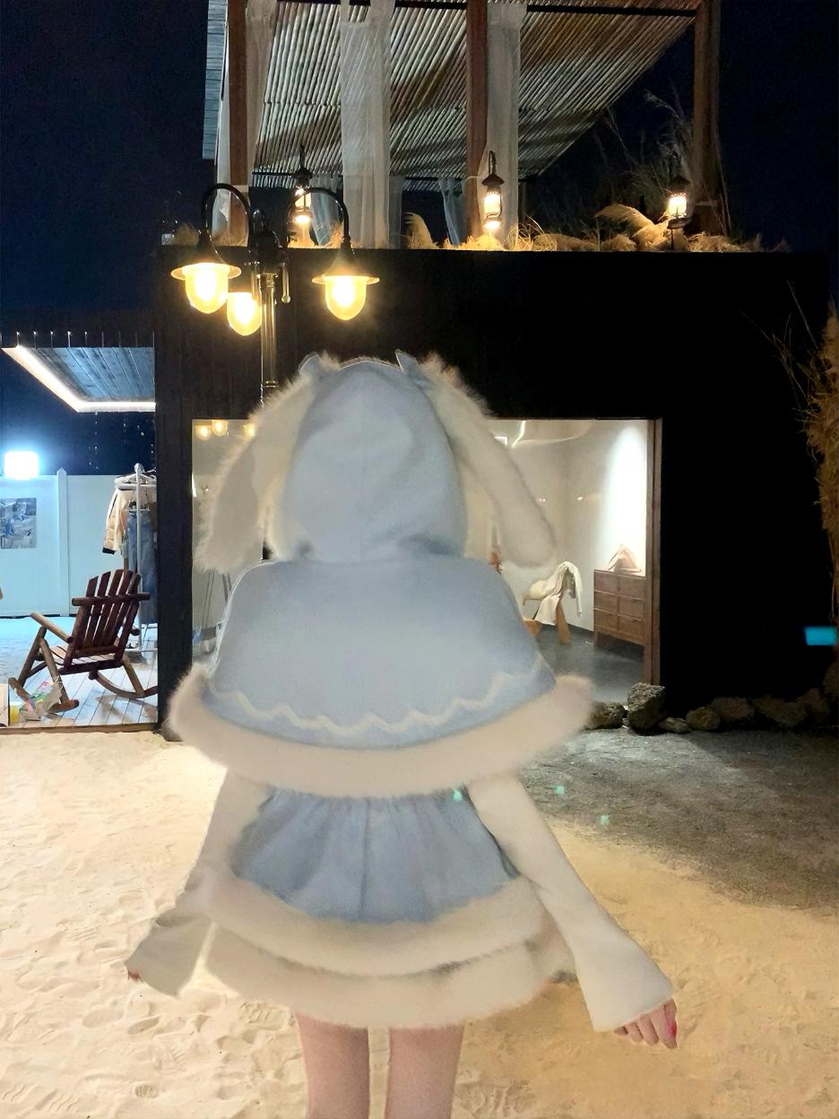 Person wearing a light blue and beige dress with a hood in an outdoor setting at night.
