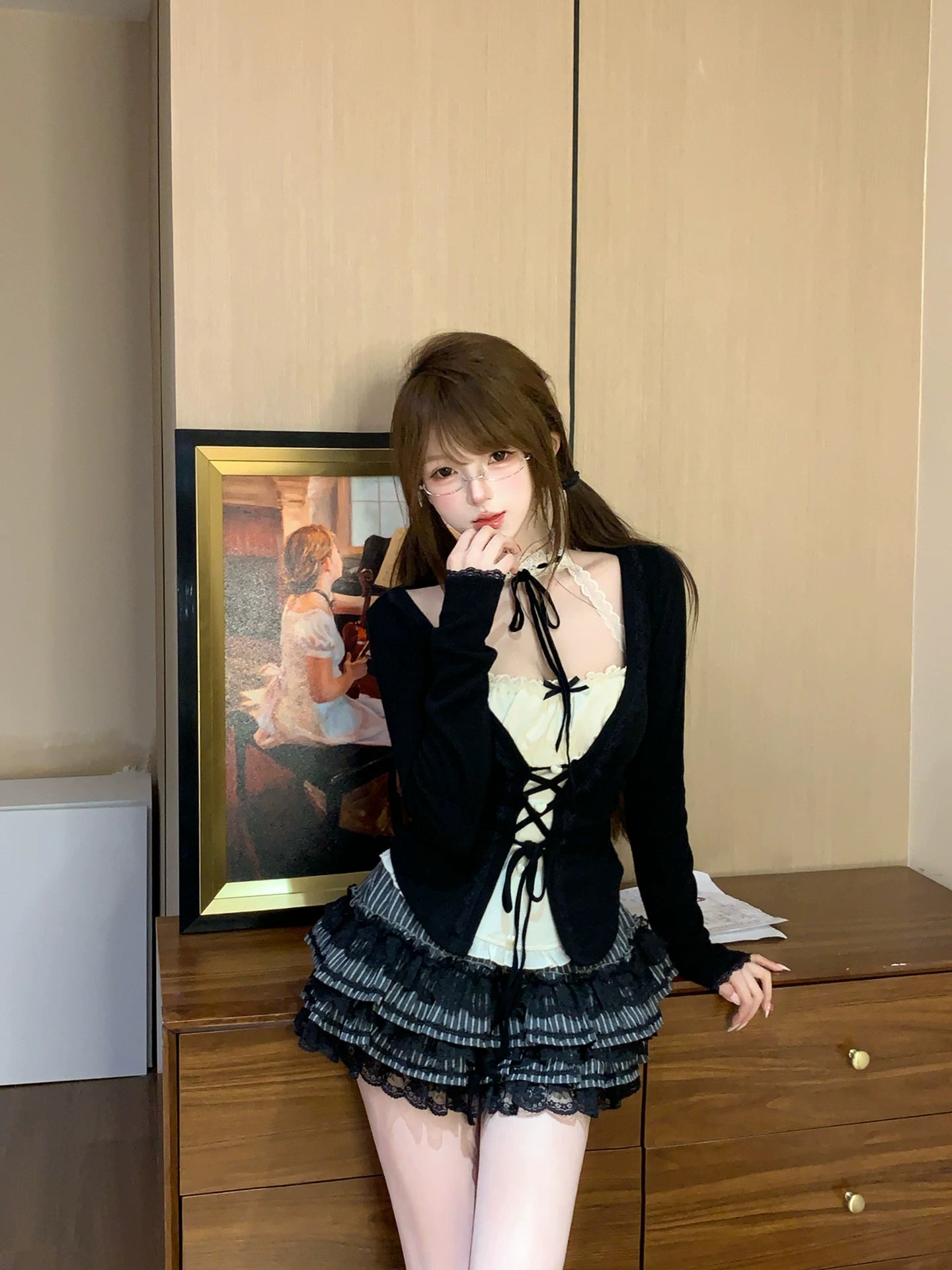 Woman in a coquette stylish outfit standing in a room with a painting on the wall.