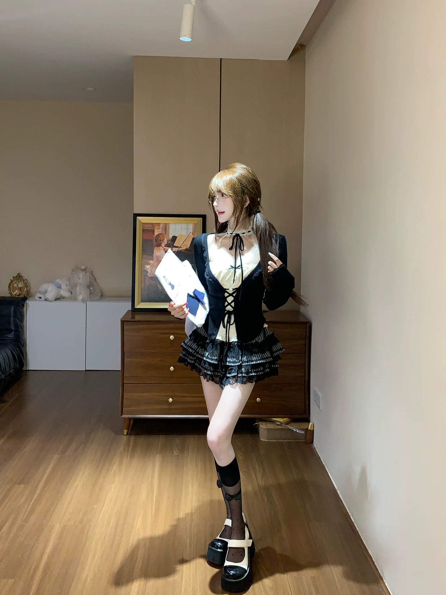 Person in a room holding a book, wearing a coquette black outfit with white accents.