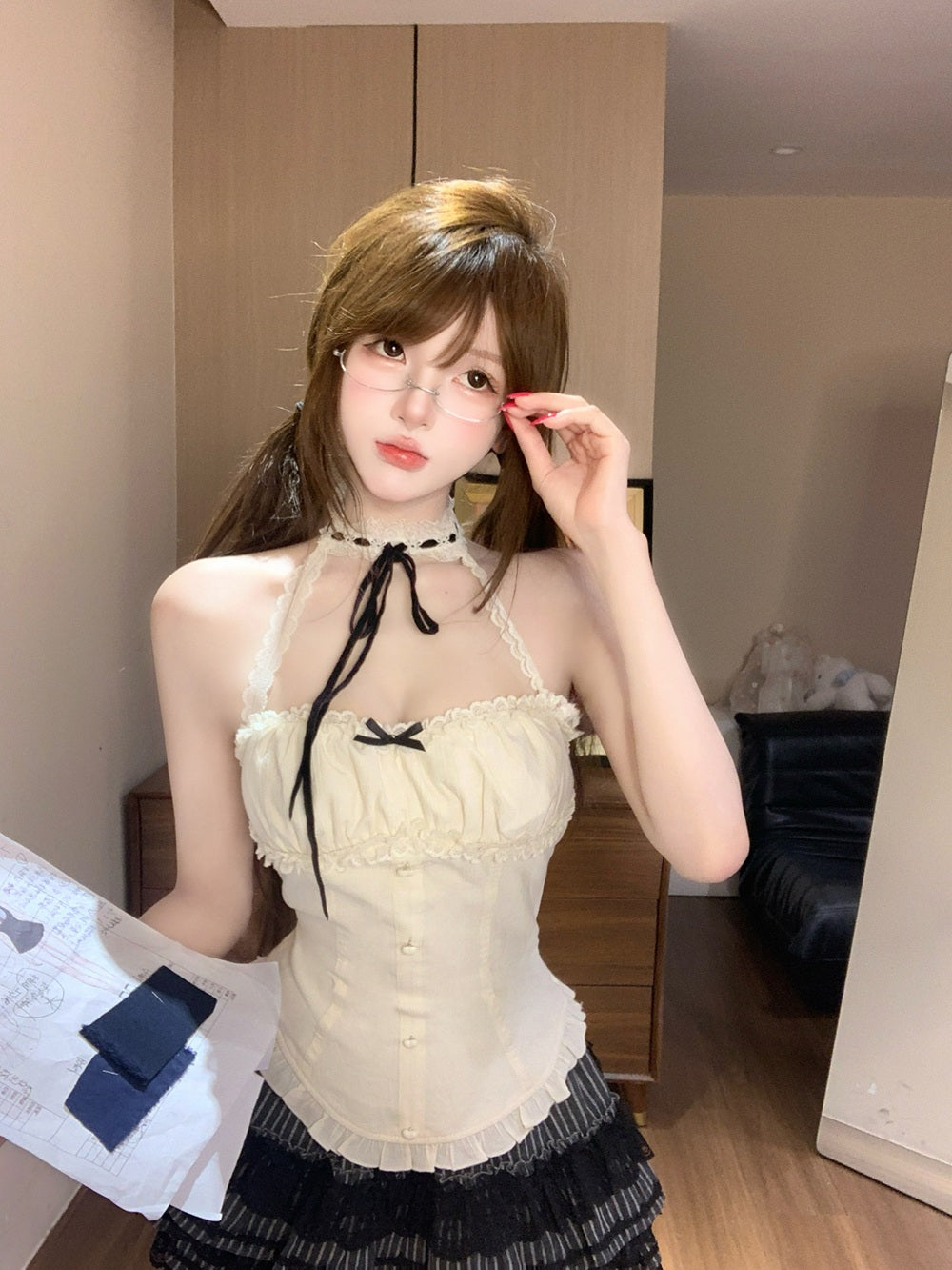 Person wearing a coquette white lace top with black ribbons in a room.