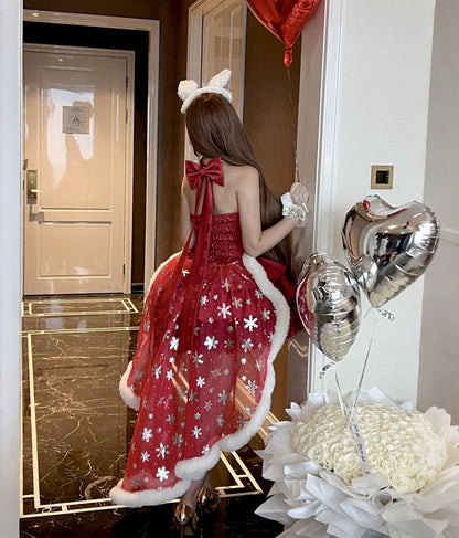 Woman in a red dress with white floral patterns and fur trim, holding silver balloons in a room.
