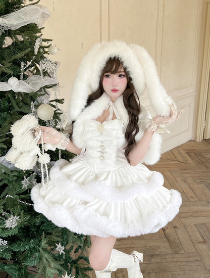 Woman in a white dress with fur trim standing next to a decorated Christmas tree.