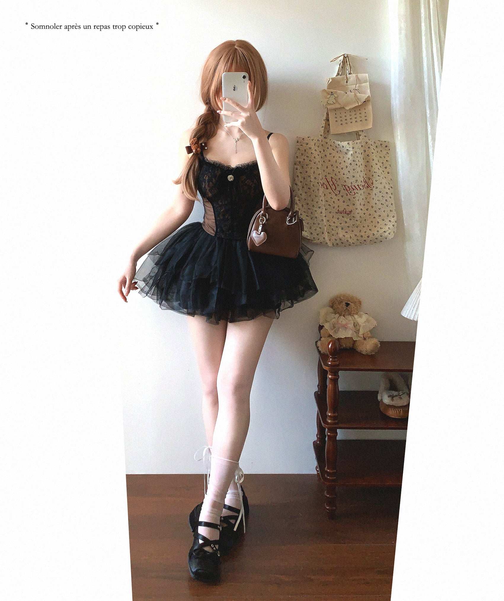 Person wearing a black dress with sheer panels, standing in a room with a teddy bear and handbag on a shelf.