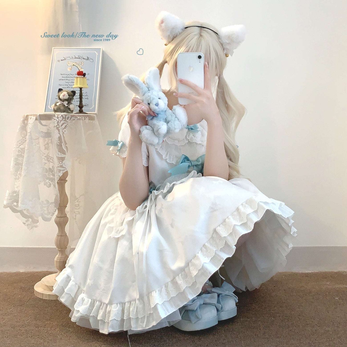 Person in a white dress with cat ears taking a selfie in a room.