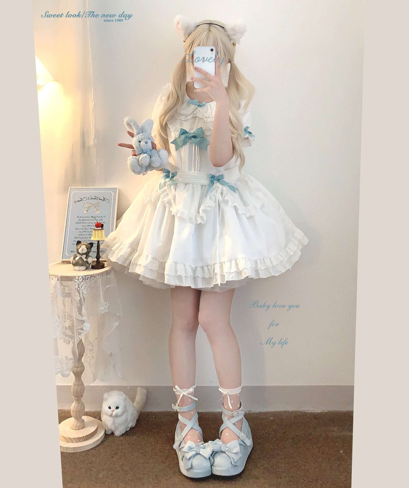 Person wearing a white dress with blue accents, holding a plush toy, in a room setting.