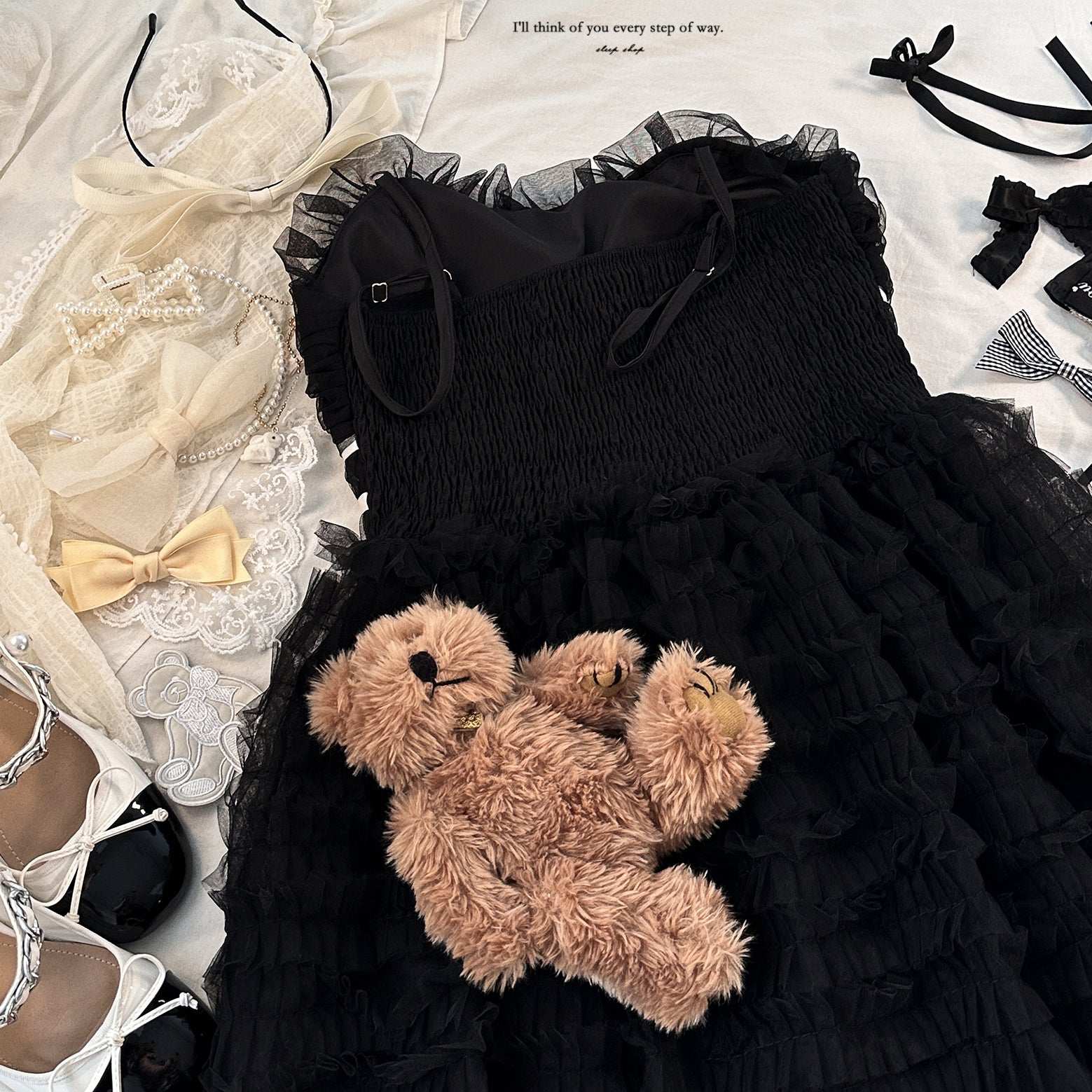 Black dress with a teddy bear toy on a white surface with accessories.