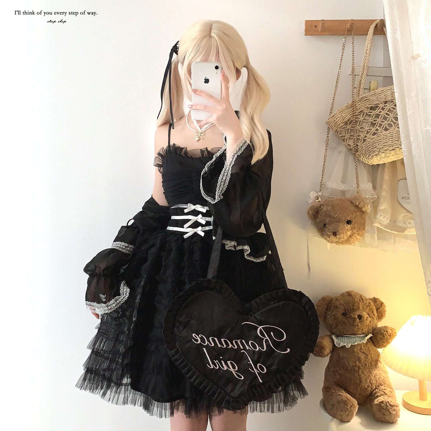 Person wearing a black lace dress with white text, standing next to teddy bears in a room.