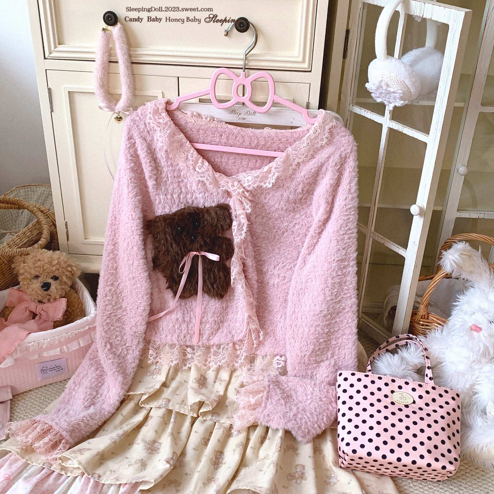 Pink cardigan with teddy bear design on a hanger in a nursery setting.
