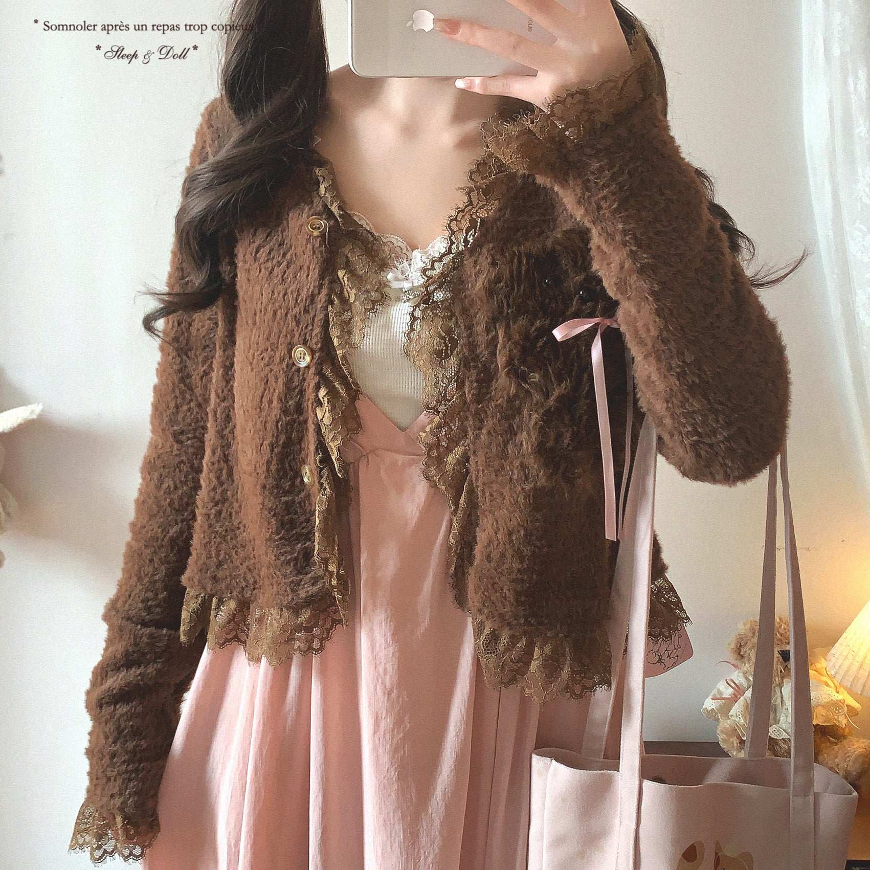 Person wearing a brown textured cardigan over a pink dress, holding a phone.