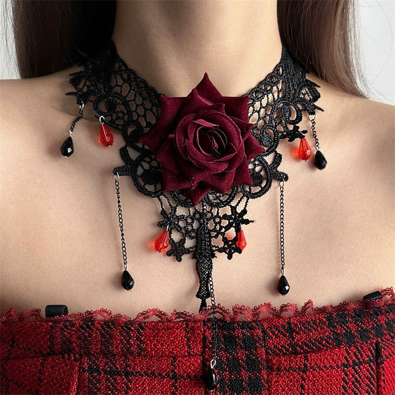 Black lace choker with a red rose and red teardrop pendants on a person wearing a red and black checkered top.