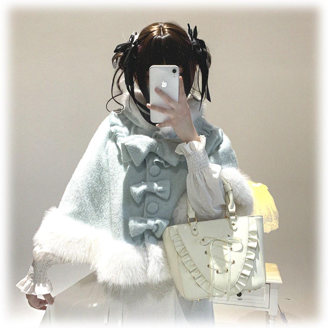 Person wearing a light blue vest with large bows and white fur trim, holding a phone.