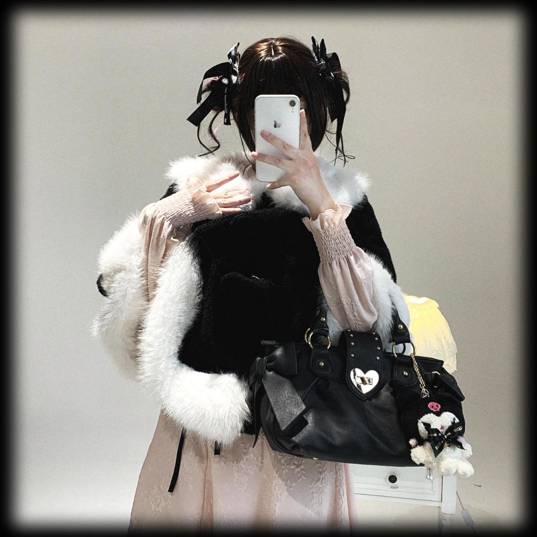 Person wearing a black coat with white fur trim, holding a phone and a black bag with heart-shaped decorations.