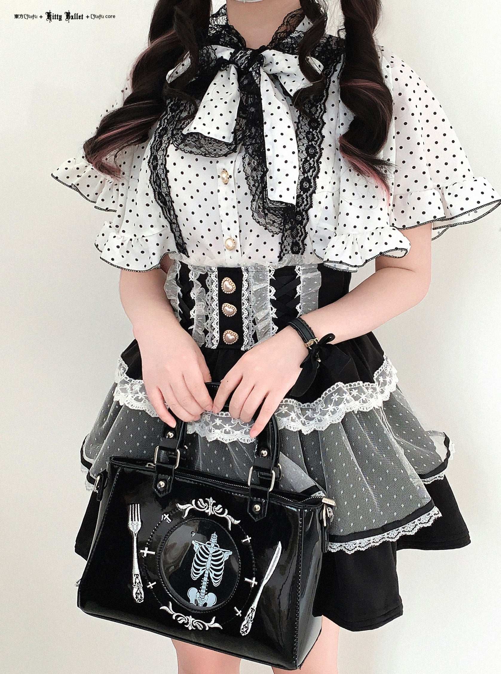 Person wearing a black and white polka dot dress with a skeleton design handbag.