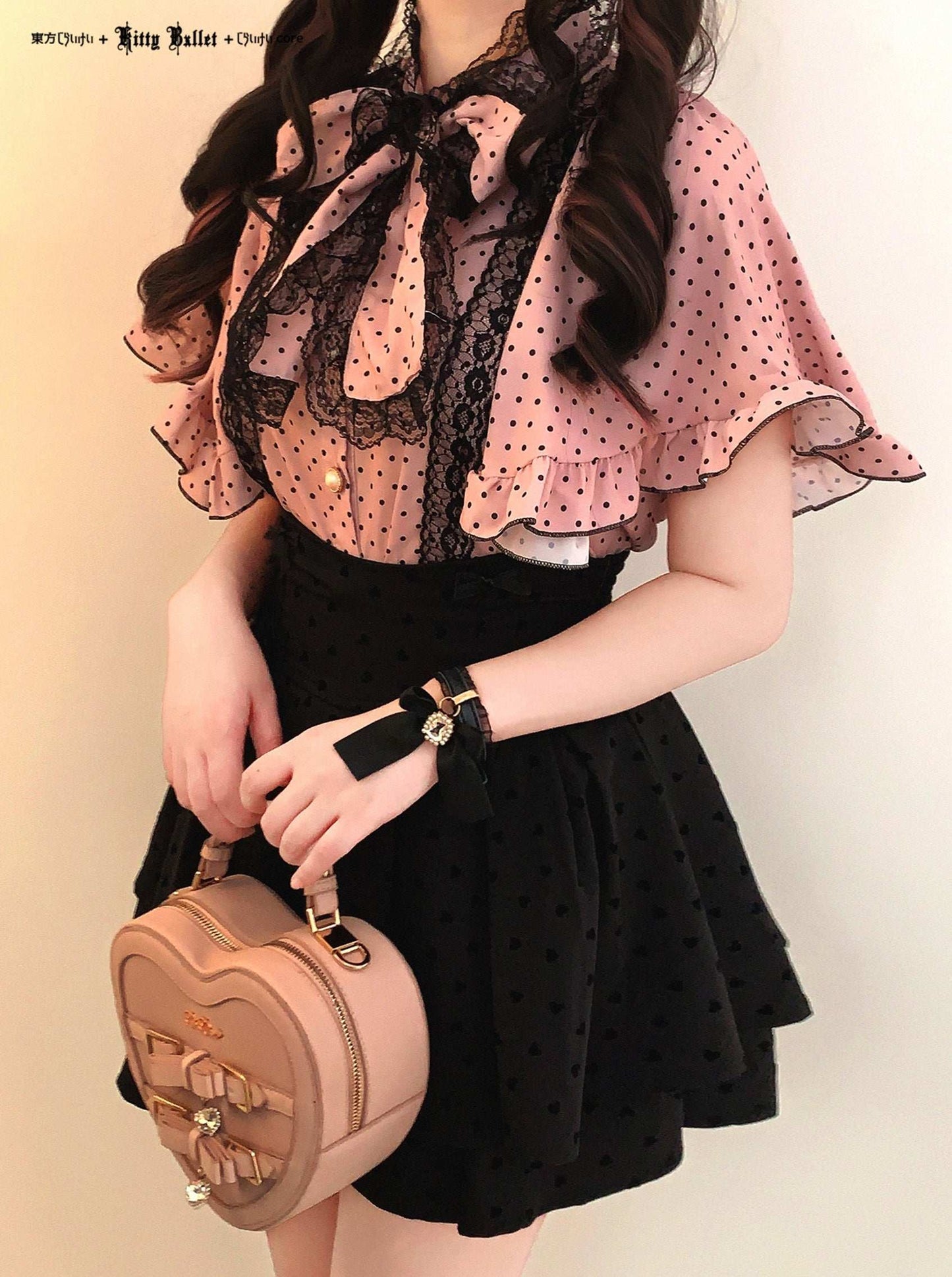 Person wearing a polka dot blouse with a large bow and holding a small bag against a plain background