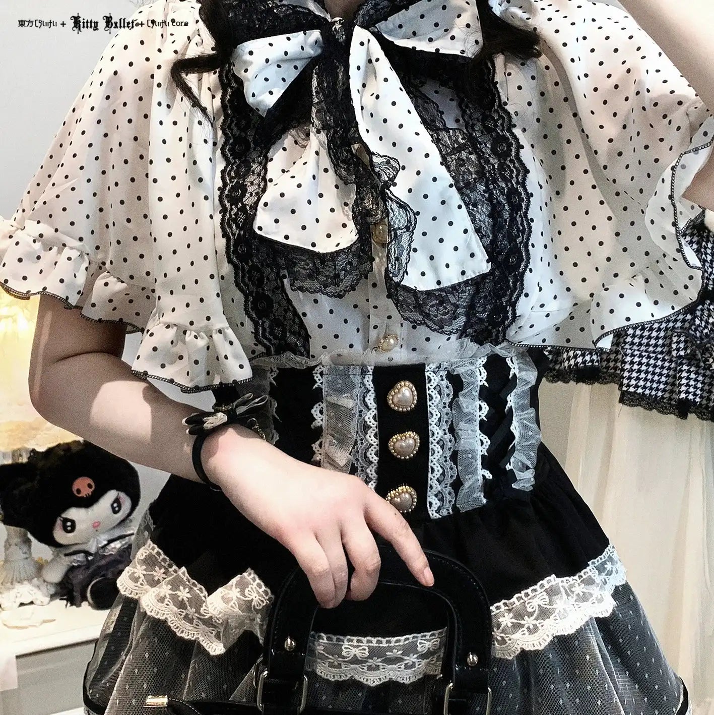 Person wearing a detailed black and white outfit with lace and polka dots, holding a handbag.
