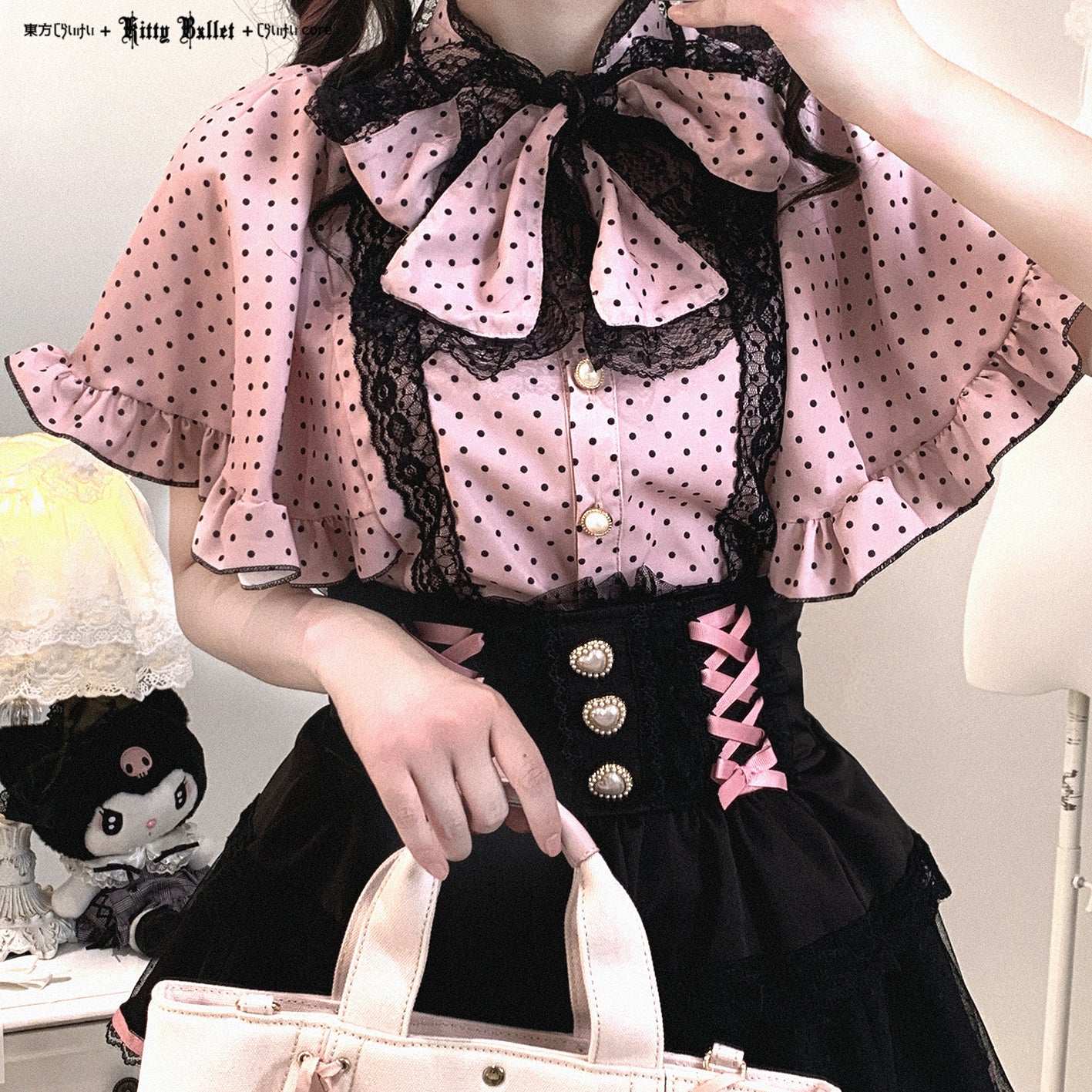 Person wearing a pink polka dot blouse with black lace details and a black skirt.