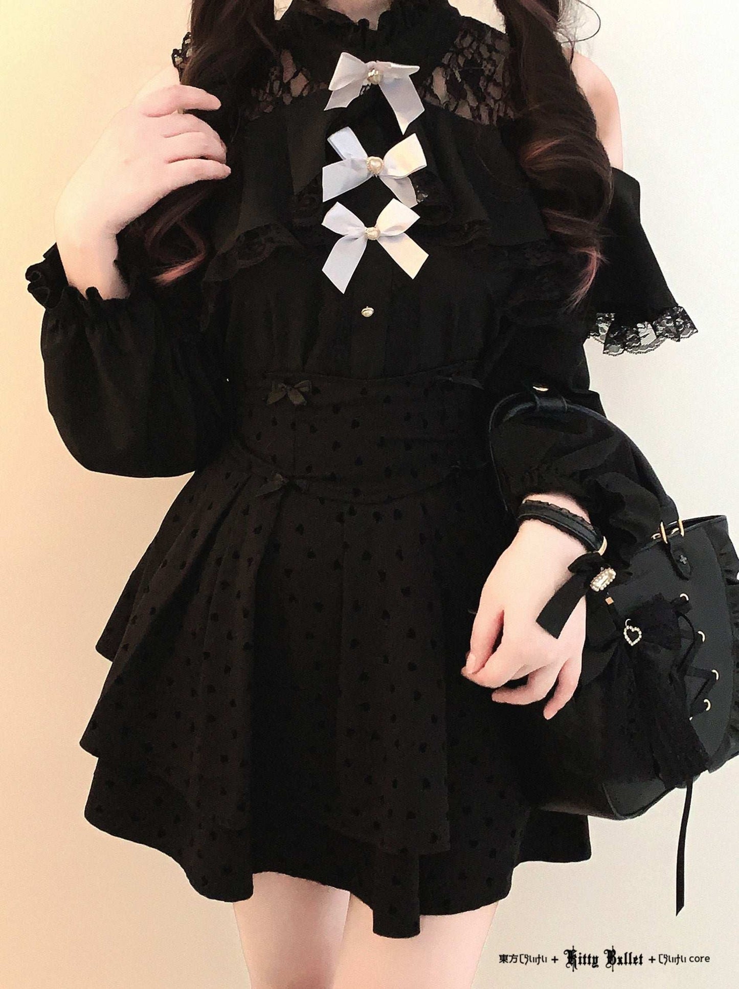 Person wearing a black polka dot dress with white bows and holding a black bag against a beige background