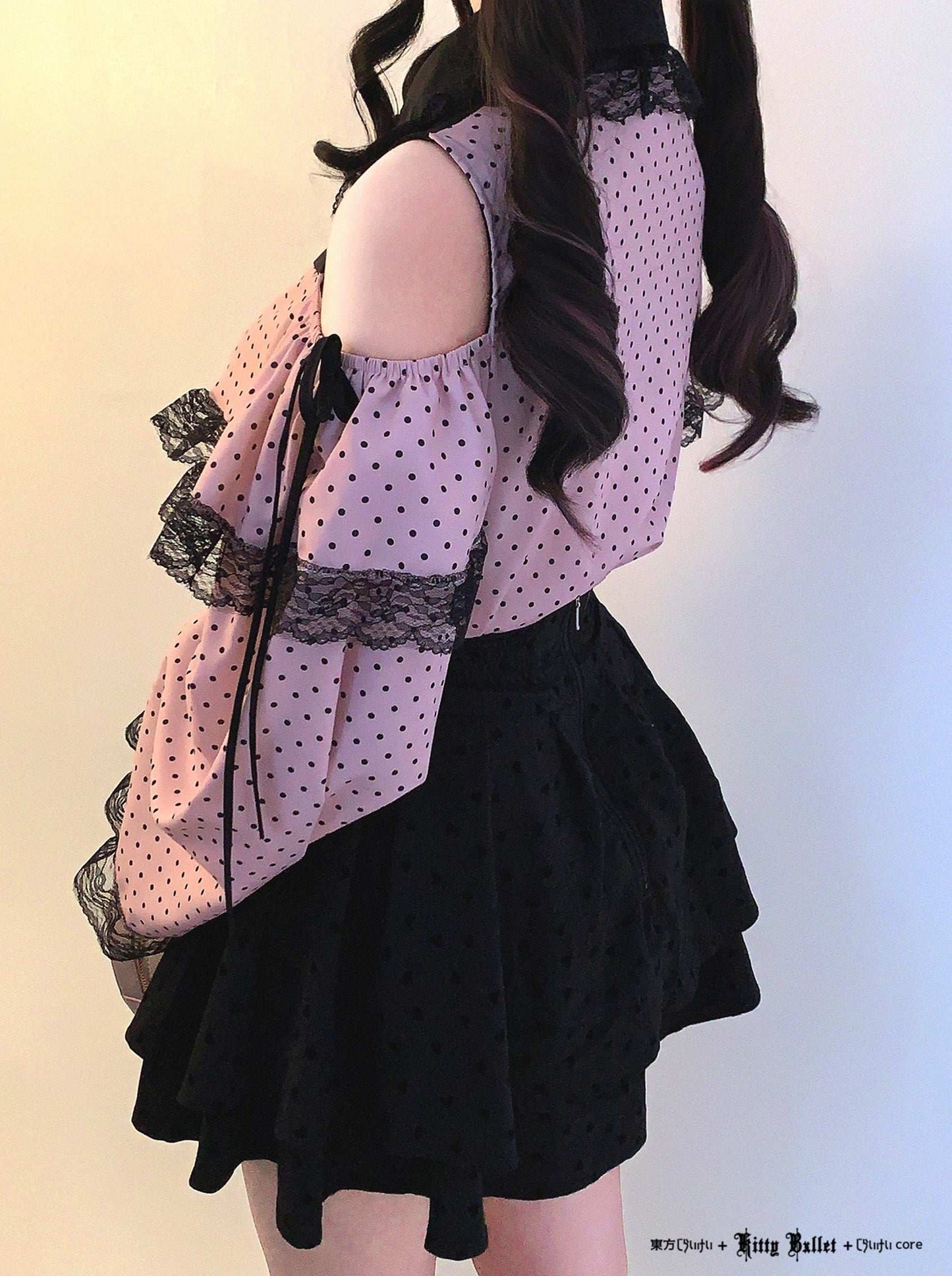 Person wearing a polka dot blouse with lace details and a black skirt on a gradient background.