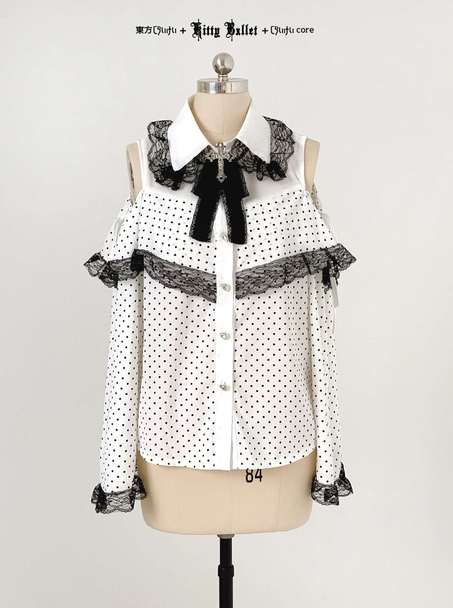 White blouse with black polka dots and lace details on a mannequin against a white background.
