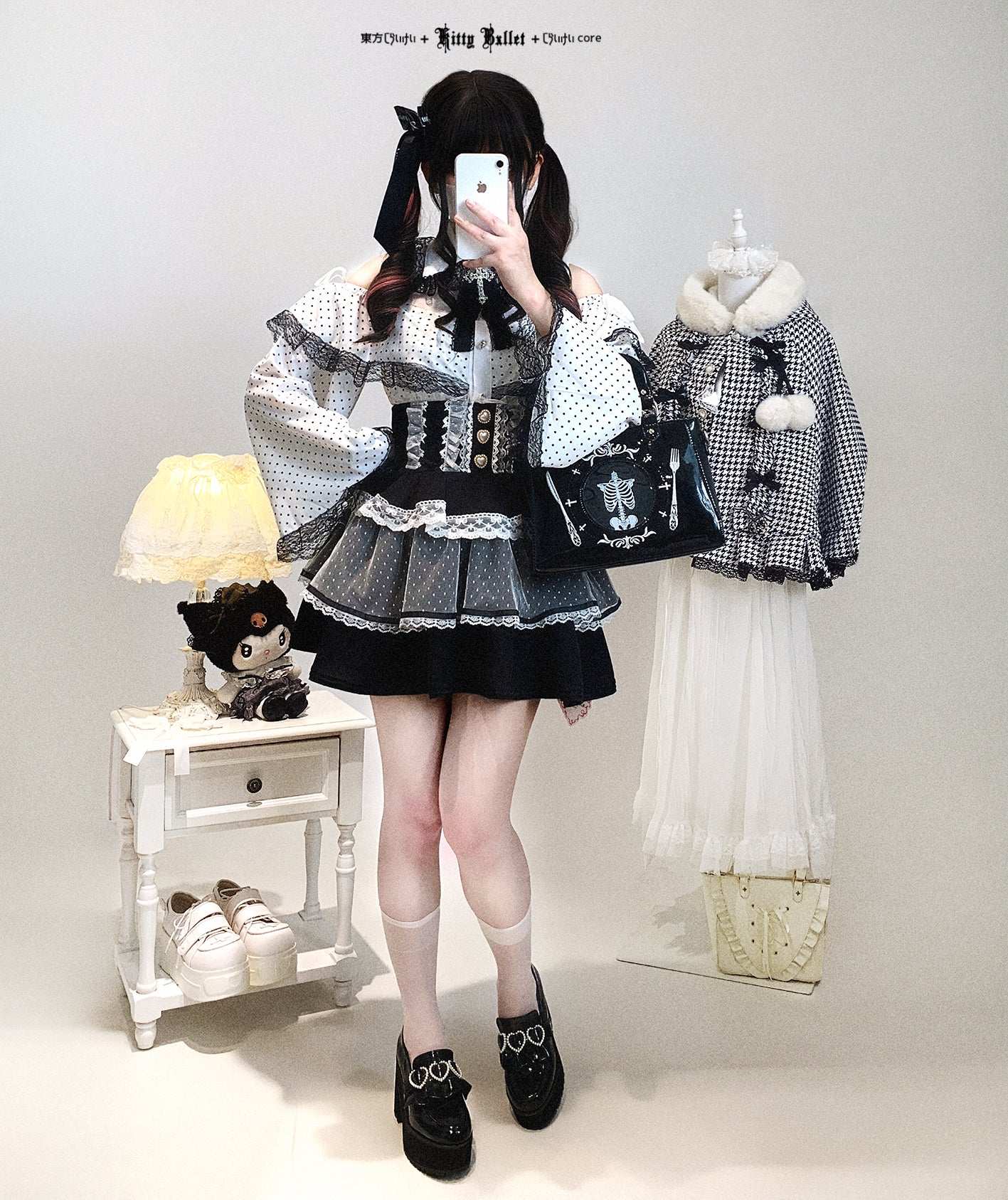 Person wearing a black and white outfit with a skirt and top, standing in a room with a lamp and small table.