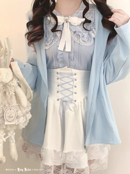 Person wearing a light blue jacket over a white dress with lace details on a neutral background