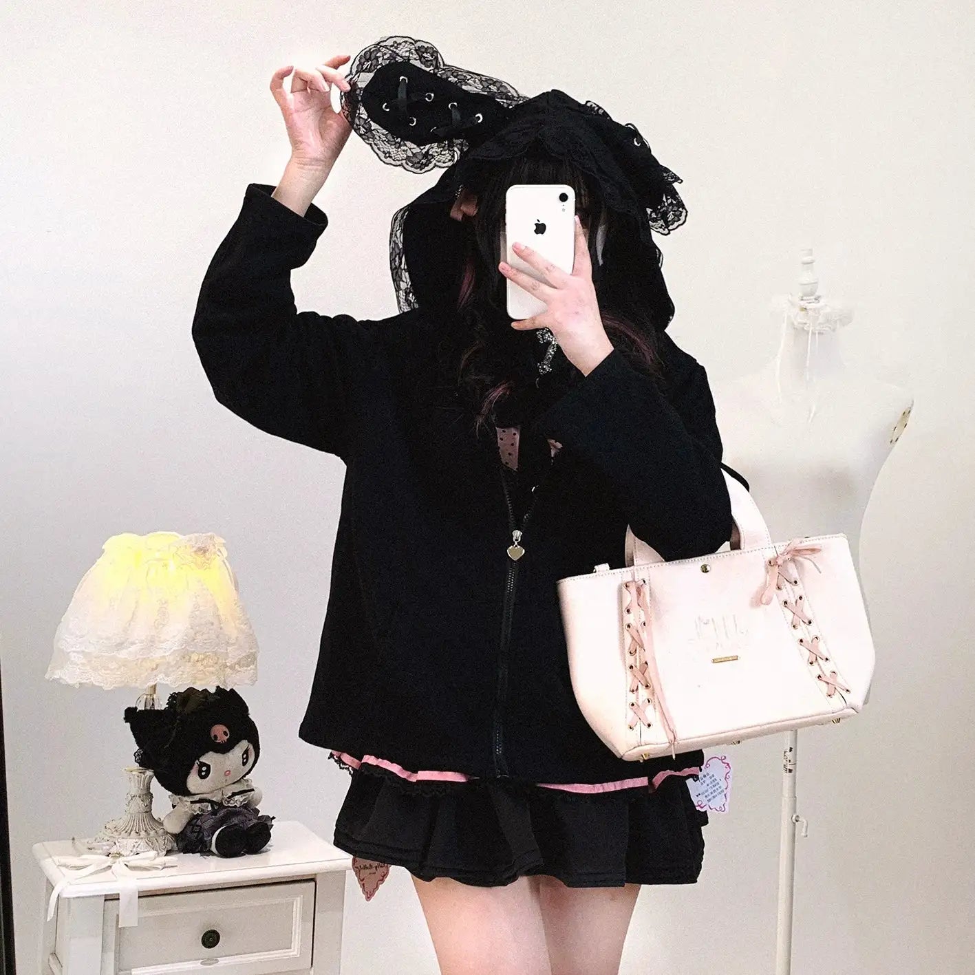 Person in black outfit with pink accents holding a white handbag, taking a mirror selfie.